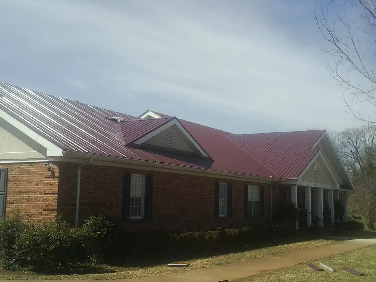 Red metal roof with gabled entries on a long brick building, from a Hail Damage Roof Repair job in Arcola