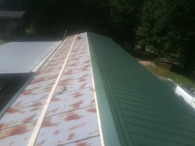 Old rusted panels beside newly installed green metal roofing — Wind Damage Roof Repair by Roofing Brothers in Arcola