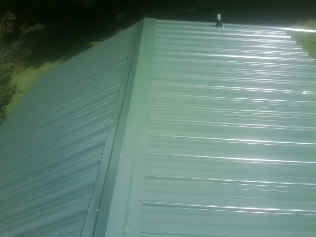 New green metal panels meeting at the ridge of a roof — Flat Roof Repair work by our crew in Arcola