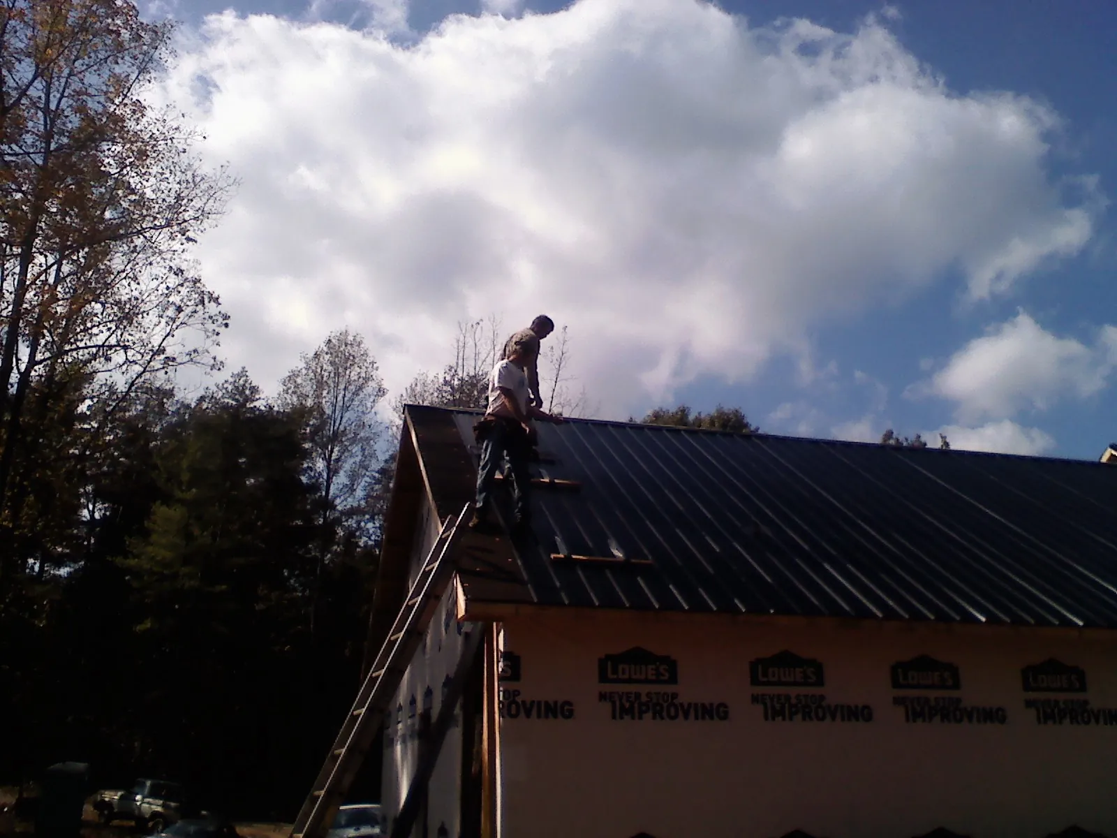 Roofer fastening dark metal panels high against a cloudy sky, from a Roof Inspection job in Arcola