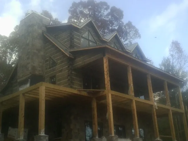 Stone chimney and dormers on a large log home with a timber porch in Arcola