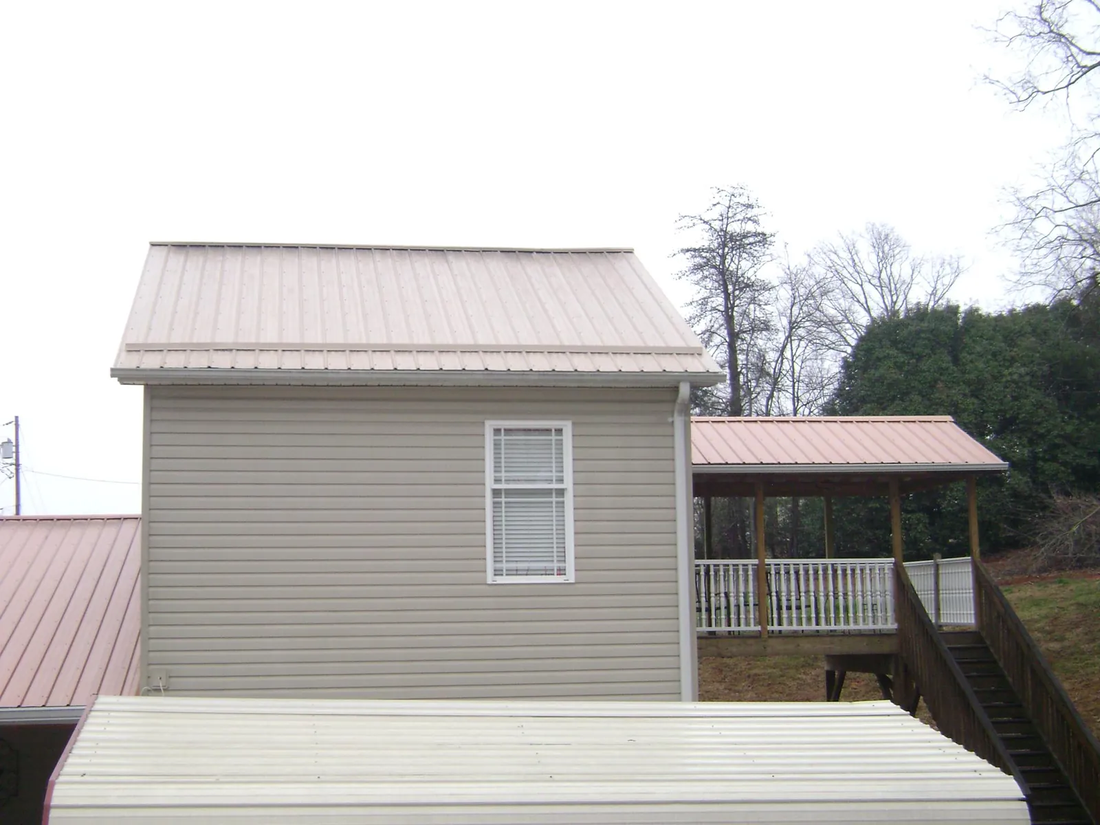 Tan metal roofs on a two story addition and attached porch, from a Roof Replacement job in Arcola